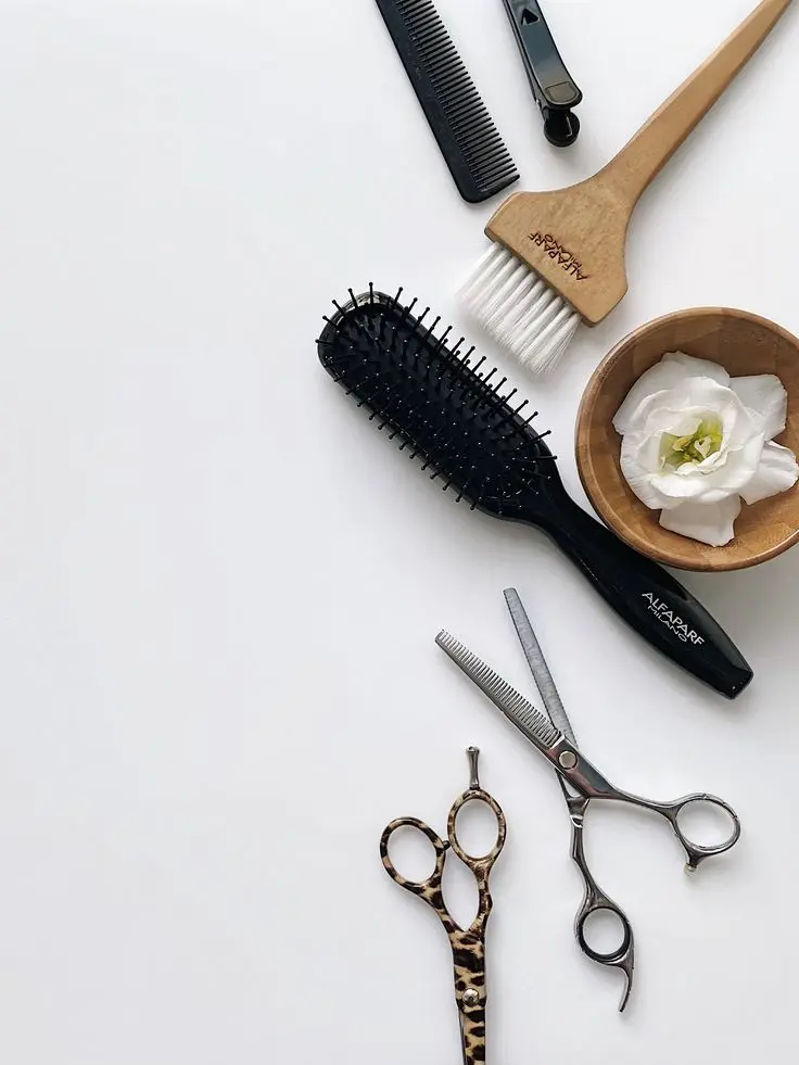 Peinetas, cepillos y tijeras sobre una mesa blanca junto a una flor